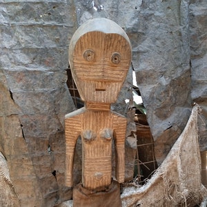 Puede incluir: Una escultura de madera de una persona con una forma humana simplificada. La escultura está tallada con detalles en la cara, el torso y los brazos. La escultura lleva una falda marrón.