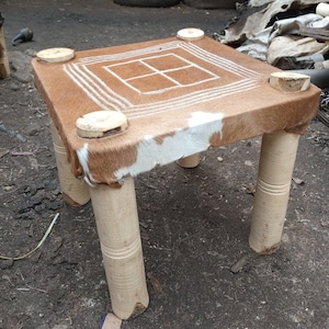 May include: A small, square table with four wooden legs. The tabletop is covered in a brown and white cowhide with a geometric pattern.