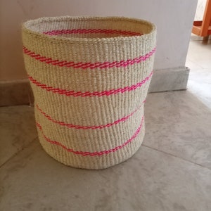 May include: A woven basket with pink stripes. The basket is made of natural fibers and has a cylindrical shape.