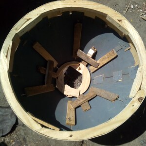 Puede incluir: Un marco redondo de madera con una superficie circular gris en el interior. El marco est&aacute; hecho de tablones de madera y tiene una abertura circular en el centro. La superficie dentro del marco est&aacute; hecha de un material gris oscuro y tiene una serie de listones de madera dispuestos en un patr&oacute;n radial.