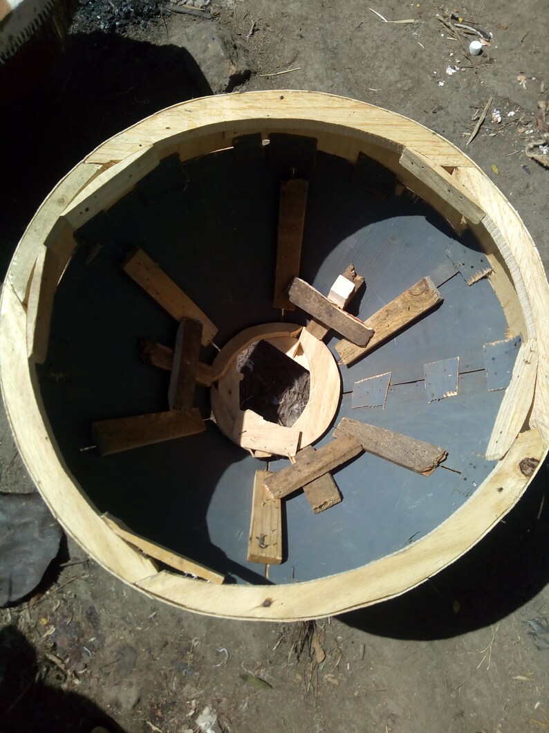 Puede incluir: Un marco redondo de madera con una superficie circular gris en el interior. El marco est&aacute; hecho de tablones de madera y tiene una abertura circular en el centro. La superficie dentro del marco est&aacute; hecha de un material gris oscuro y tiene una serie de listones de madera dispuestos en un patr&oacute;n radial.