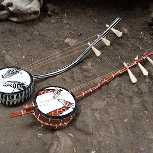 Könnte beinhalten: Zwei traditionelle afrikanische Saiteninstrumente, bekannt als Kora, mit einem runden Holzkörper und einem langen Hals. Eine Kora ist mit einem Zebra-Muster verziert, während die andere mit einem Giraffen-Muster verziert ist.