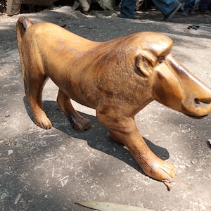 May include: A wooden sculpture of a baboon, carved in a realistic style. The sculpture is brown and has a detailed face with a long snout.