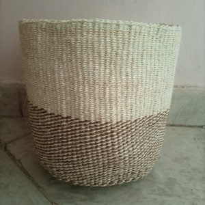 May include: A woven basket with a natural brown and white color scheme. The basket is made of natural fibers and has a rounded shape.