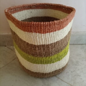 May include: A woven storage basket with a brown, white, and green striped pattern. The basket is made of natural fibers and has a cylindrical shape.