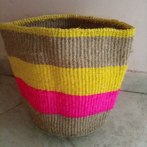 May include: A woven storage basket with brown, yellow, and pink stripes. The basket is made of natural fibers and has a cylindrical shape.