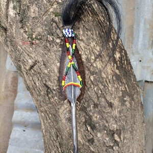 May include: A decorative spear with a black feather and colorful beads. The spear is made of metal and has a wooden handle.