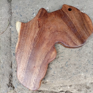 Könnte beinhalten: Ein Schneidebrett aus Holz in Form des afrikanischen Kontinents. Das Brett ist aus dunkelbraunem Holz mit natürlicher Maserung.