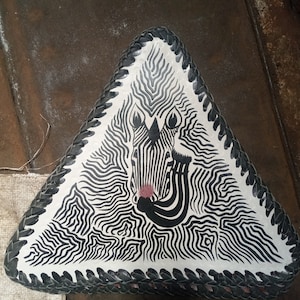 May include: A triangular leather cushion with a black and white zebra pattern and a black braided border.