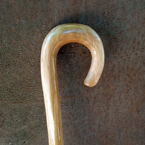 May include: A wooden walking stick with a smooth, rounded handle. The handle is a light brown color and has a slight curve.