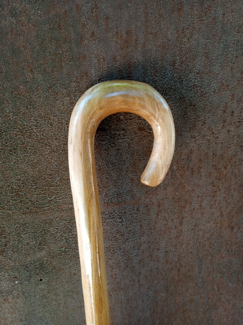 May include: A wooden walking stick with a smooth, rounded handle. The handle is a light brown color and has a slight curve.