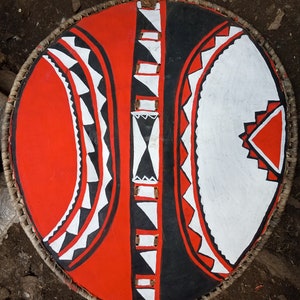 May include: A round shield with a woven edge, painted in red, black, and white geometric patterns.