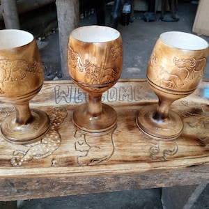Puede incluir: Tres tazas de madera con diseños de animales tallados se muestran en una bandeja de madera con la palabra "WELCOME" tallada en ella.