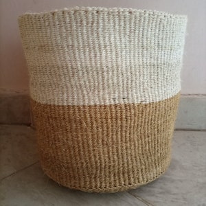 May include: A woven storage basket with a natural brown bottom and a white top. The basket is made of natural fibers and has a cylindrical shape.