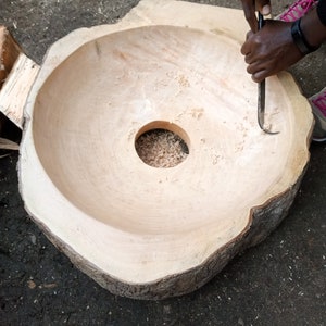 May include: A person carving a large wooden bowl with a chisel. The bowl is made from a tree trunk and has a circular opening in the center.