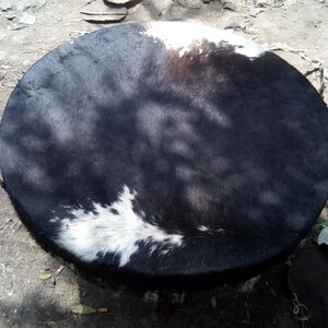 Puede incluir: Un parche de tambor de piel de vaca negro y blanco, con un parche blanco en el centro. El parche del tambor est&aacute; estirado y listo para ser usado.