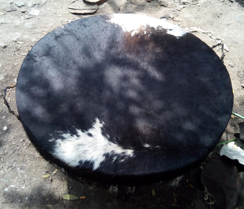 Puede incluir: Un parche de tambor de piel de vaca negro y blanco, con un parche blanco en el centro. El parche del tambor est&aacute; estirado y listo para ser usado.
