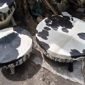 Puede incluir: Tres taburetes redondos de piel de vaca con parches negros y blancos. Los taburetes tienen una franja alrededor del borde y est&aacute;n sostenidos por patas de madera.