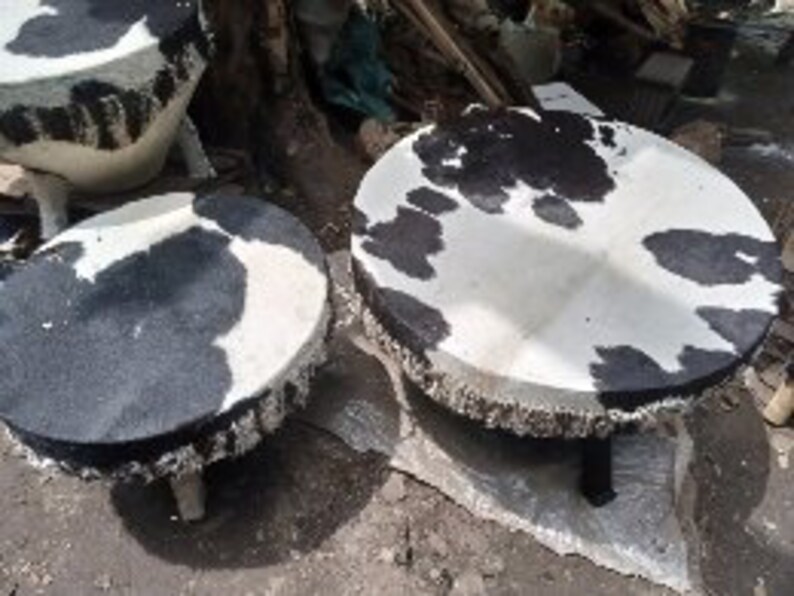 Puede incluir: Tres taburetes redondos de piel de vaca con parches negros y blancos. Los taburetes tienen una franja alrededor del borde y est&aacute;n sostenidos por patas de madera.