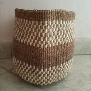 May include: A brown and white woven basket with a geometric pattern. The basket is made of natural fibers and has a cylindrical shape.