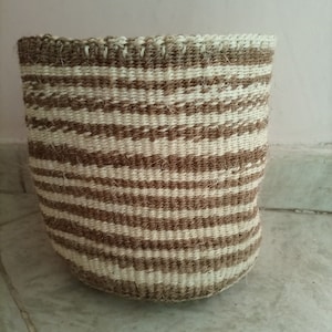 May include: A woven basket with brown and white stripes. The basket is made of natural fibers and has a cylindrical shape.