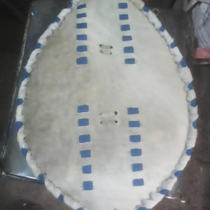 May include: A white leather shield with blue trim and stitching. The shield is oval shaped and has a fringed edge.