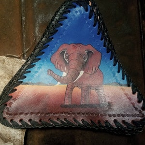 May include: A triangular leather seat cushion with a black braided trim. The cushion features a painted image of an elephant in a desert landscape.