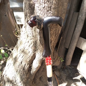 Puede incluir: Un bastón de madera con una cabeza de león tallada en la parte superior. El bastón está pintado de negro y tiene detalles rojos y blancos.