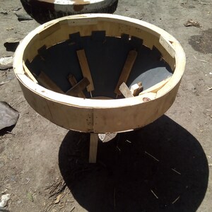 Puede incluir: Un molde de madera para hacer macetas de hormig&oacute;n. El molde est&aacute; hecho de madera contrachapada y tiene una parte superior circular con un fondo en forma de embudo. El molde est&aacute; sobre una superficie de tierra.