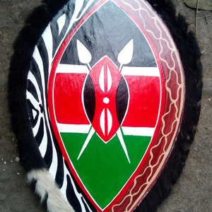 May include: A shield with a black, white, and red zebra pattern on the outer edge. The center of the shield features the flag of Kenya, with red, black, green, and white colors. The shield is trimmed with black fur.