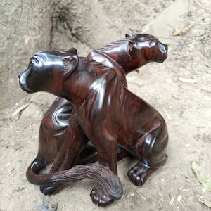 May include: A hand-carved wooden sculpture of two black panthers, one sitting on top of the other. The sculpture is made of dark wood and has a polished finish.