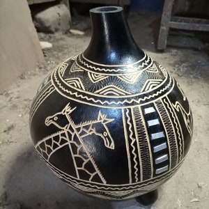 May include: Black gourd vase with intricate carvings of geometric patterns and animal figures. The vase is decorated with a light brown color and has a shiny finish.