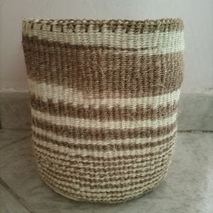 May include: A woven basket with brown and white stripes. The basket is made of natural fibers and has a cylindrical shape.