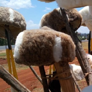 May include: A collection of brown and white fuzzy hats with white stripes on a wooden stick. The hats are made of sheepskin and are displayed outdoors.