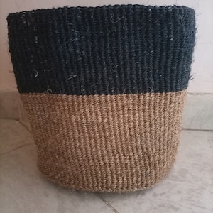 May include: A black and brown woven basket with a cylindrical shape. The top half of the basket is black and the bottom half is brown.