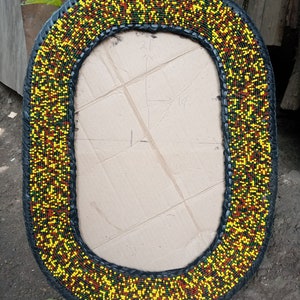 May include: Oval mirror with a black frame decorated with yellow, green, and red beads.