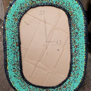 May include: A turquoise beaded oval mirror frame with black leather trim. The frame is 21 inches tall and 19 inches wide.