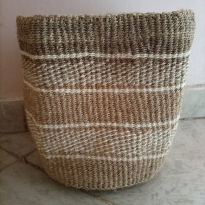 May include: A woven basket with a natural brown color and white stripes. The basket is made of natural fibers and has a round shape.