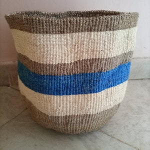 May include: A woven storage basket with a striped pattern in beige, white, and blue. The basket is made of natural fibers and has a cylindrical shape.