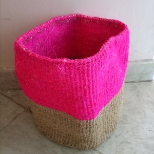 May include: A pink and brown woven basket with a round shape. The top half of the basket is pink and the bottom half is brown.
