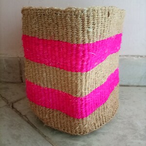 May include: A woven basket with pink stripes. The basket is made of natural fibres and has a natural brown colour.