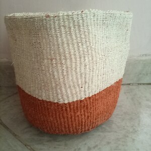 May include: A woven basket with a white top and a brown bottom. The basket is made of natural fibers and has a round shape.