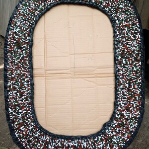 May include: Oval-shaped beaded frame with a black leather border. The frame is decorated with red, white, and green beads. The frame is approximately 21 inches by 19 inches.