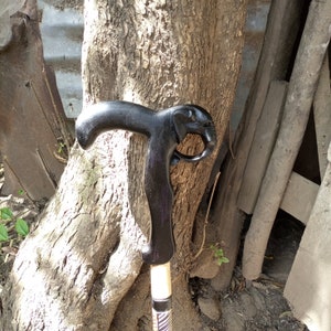 Puede incluir: Un bastón de madera negro con una cabeza de elefante tallada en el mango.