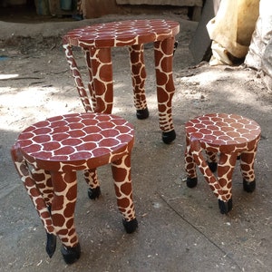 May include: Three wooden stools shaped like giraffes with brown and white spots. The stools are painted to look like a giraffe's legs and have black hooves.