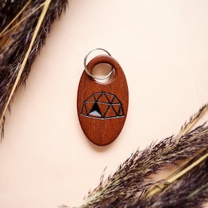 May include: A wooden keychain with a geometric design of a dome. The keychain is brown and has a silver metal ring.