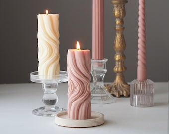 May include: Four candles, two pink and two white, with a wavy design. The candles are on a white surface with glass candle holders and a gold metal candle holder.