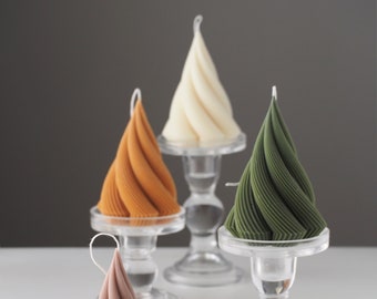 May include: A collection of spiral-shaped candles in various colors, including pink, orange, cream, and green. The candles are displayed on clear glass candle holders and a white hexagonal tray. The background is a neutral gray.