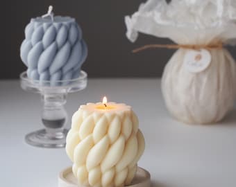 May include: Two decorative candles on separate stands. The candle on the left is blue and the candle on the right is white. Both candles are shaped like a braided rope.