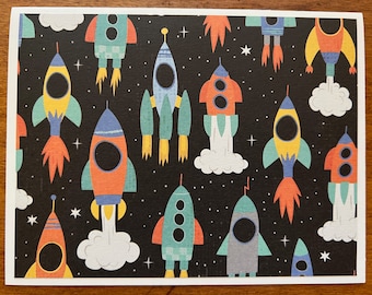 May include: A black background with a repeating pattern of colorful rockets with white clouds and stars. The rockets are in various shades of blue, green, orange, and yellow.
